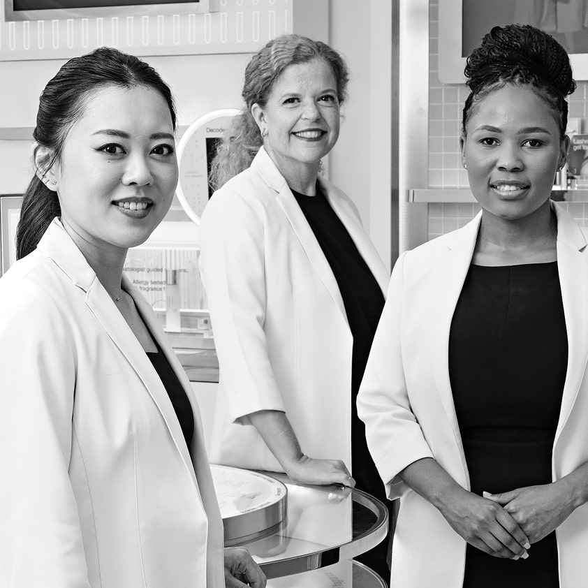 Black and white photo of 3 Clinique Consultants in a store setting wearing lab coats