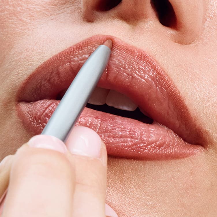 A hand applies Clinique Quickliner to lips in a soft neutral shade.