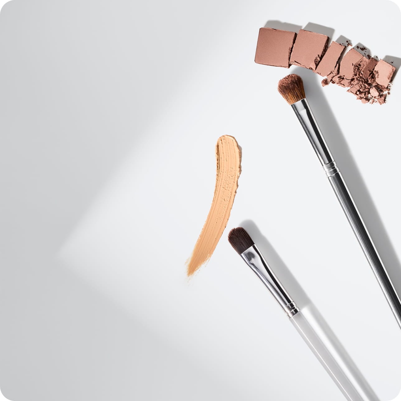 Makeup brushes shown with foundation and powder swatches against a clean white background.
