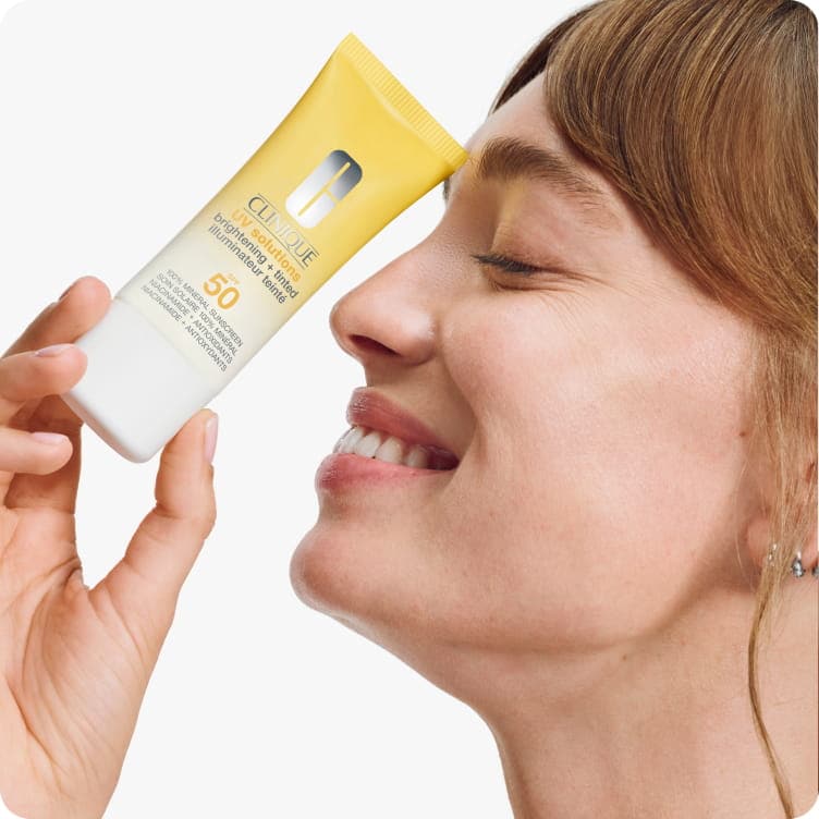Close up of model smiling holding mattifying sunscreen in a brightly lit studio. Focusing on skin texture and zero white cast.