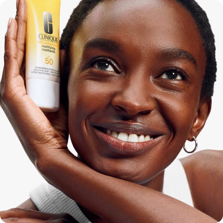Close up of model smiling holding mattifying sunscreen in a brightly lit studio. Focusing on skin texture and zero white cast.