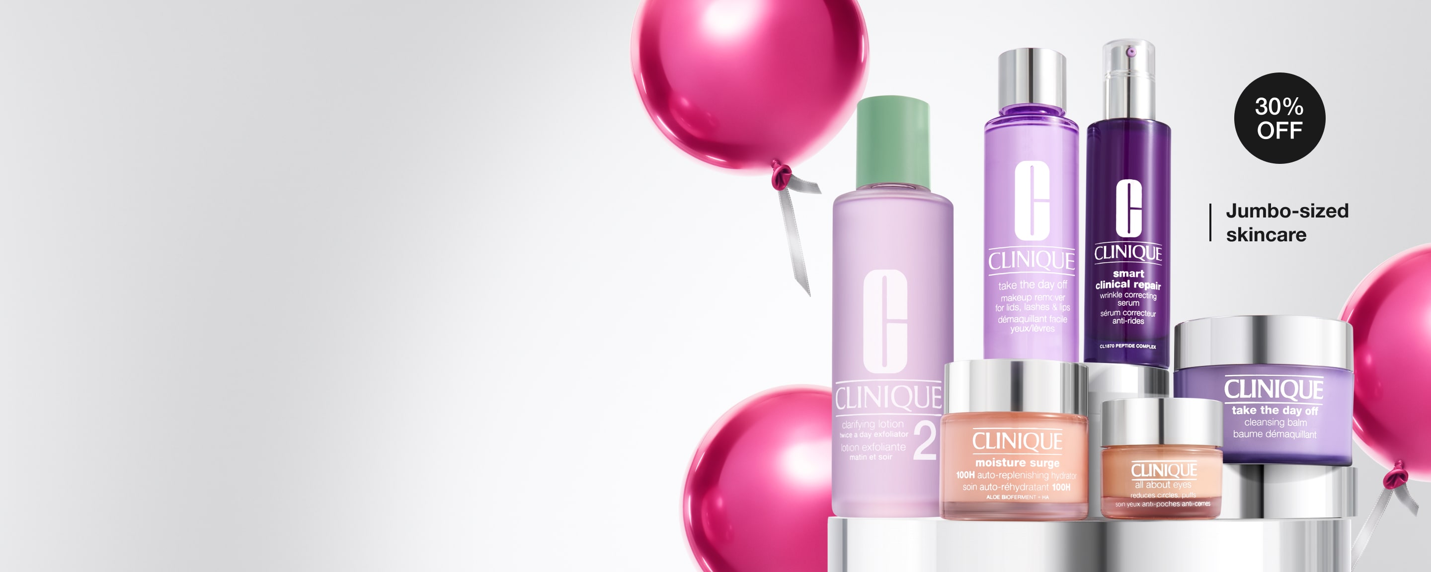 Selection of Clinique jumbo skincare products on grey plinths, with bright pink, festive balloons behind